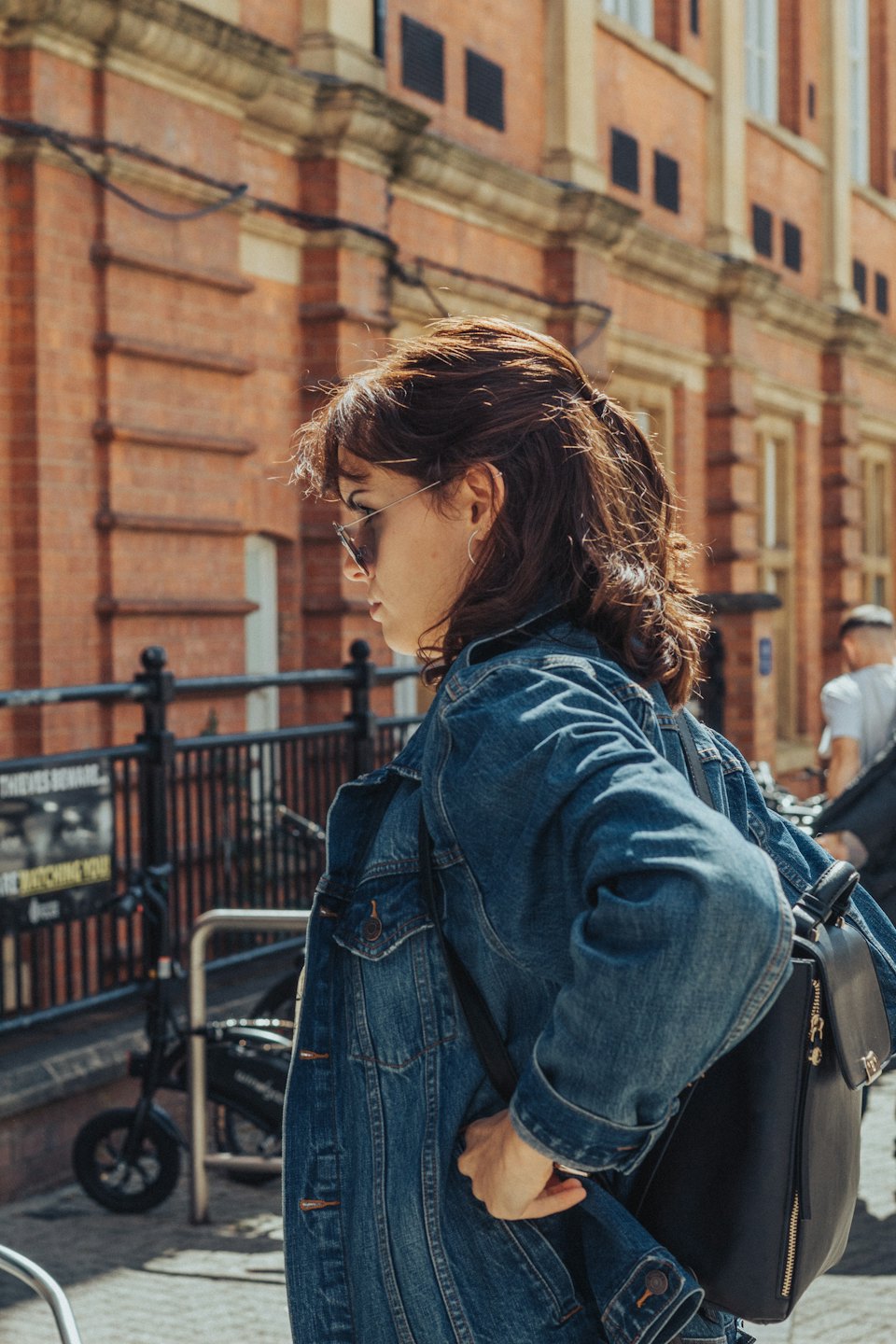 Woman walks on a sunny city street with a backpack.