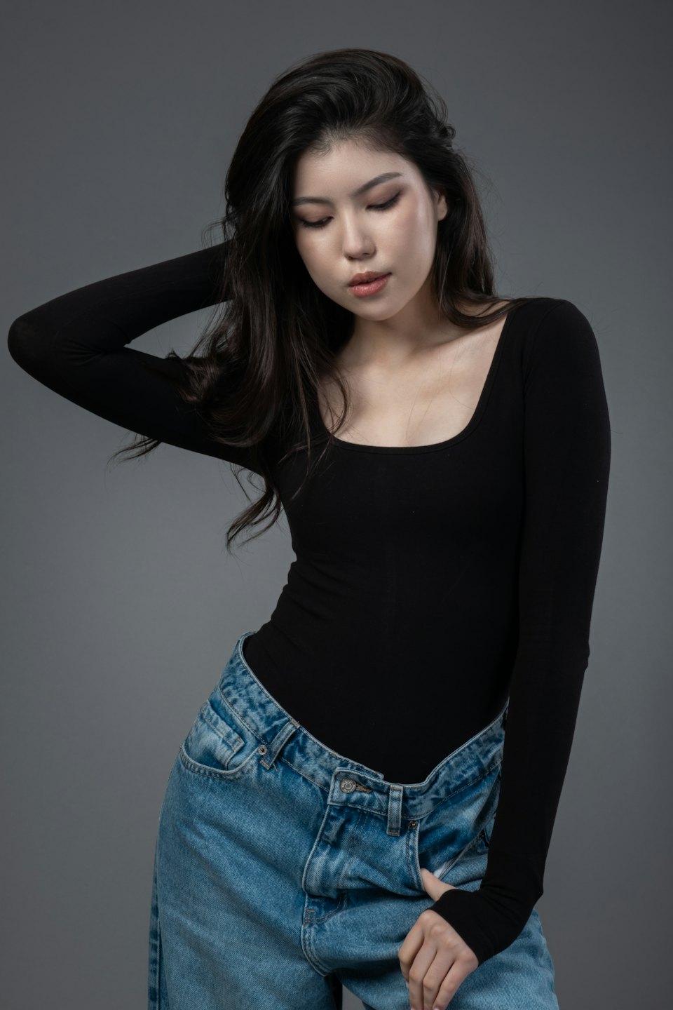 Woman in black long-sleeve shirt posing against a grey wall.