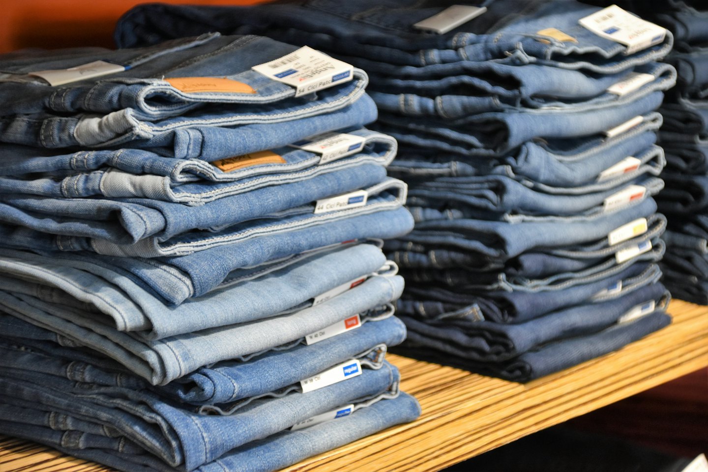 Stacks of blue denim jeans on a wooden shelf.