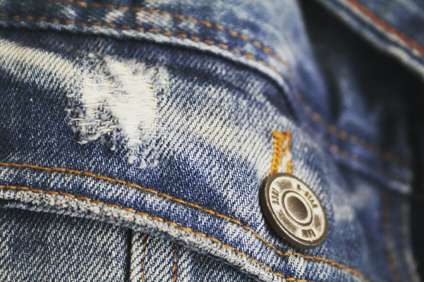 Blue denim fabric features orange stitching and a metal button.